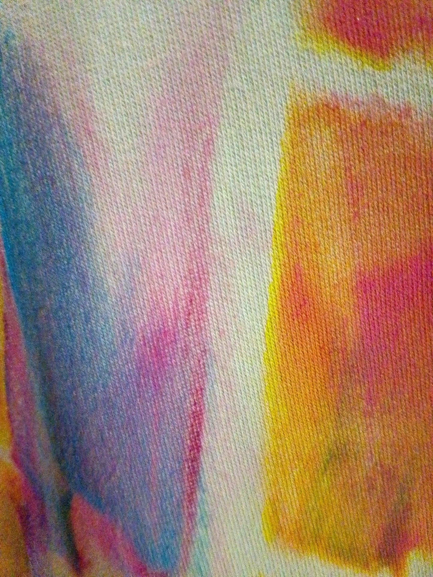 Detalle de tejido de camiseta pintada a mano con colores azul, rosa, naranja y amarillo.